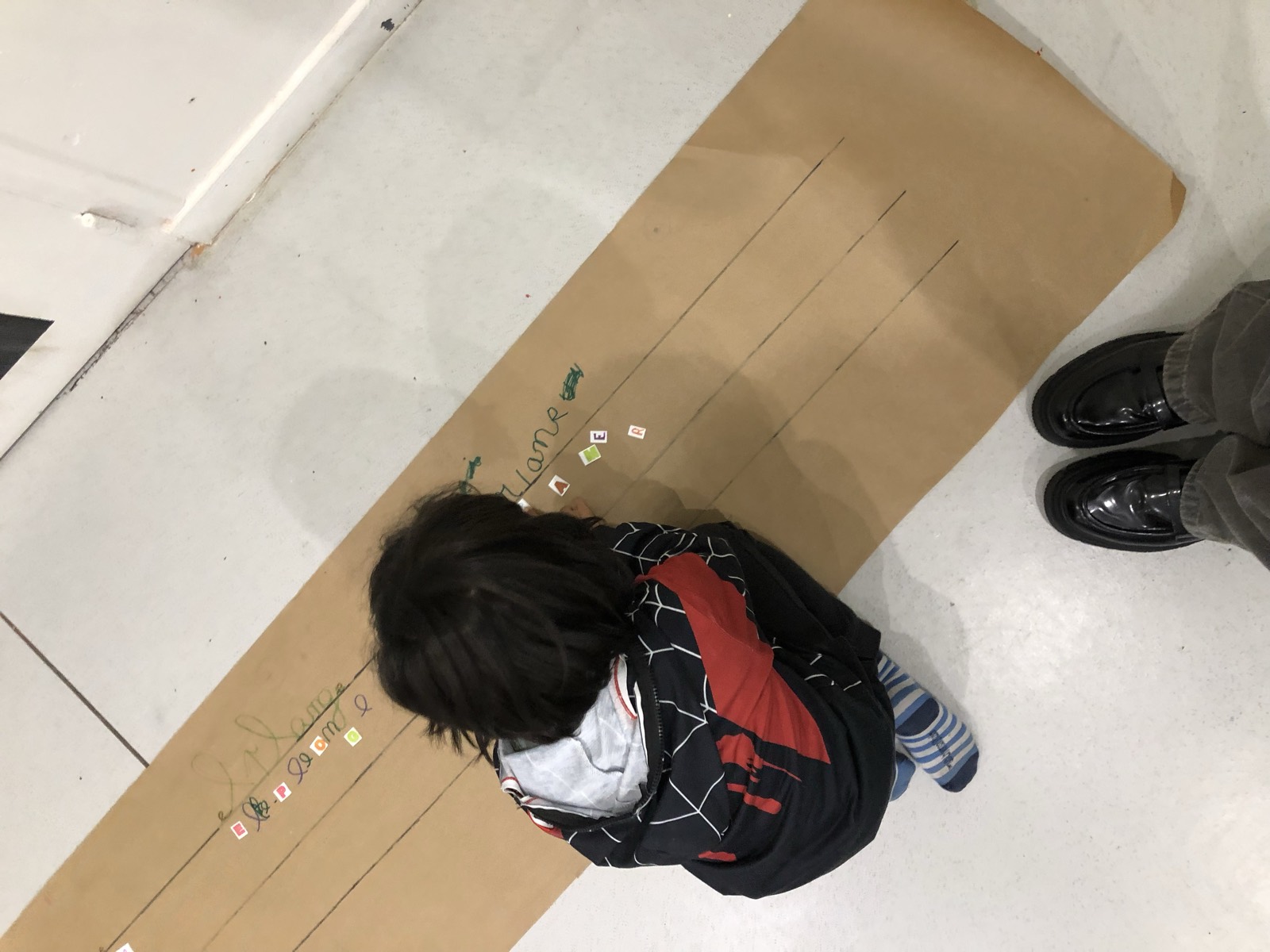 Un enfant suit une longue bande de papier posée au sol